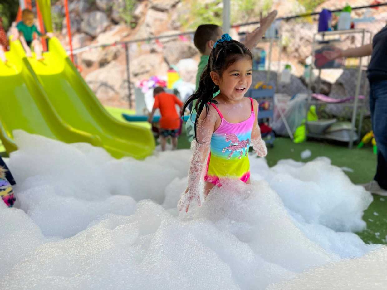 little girl playing in foam next to a slide at a guidepost montessori event oustside
