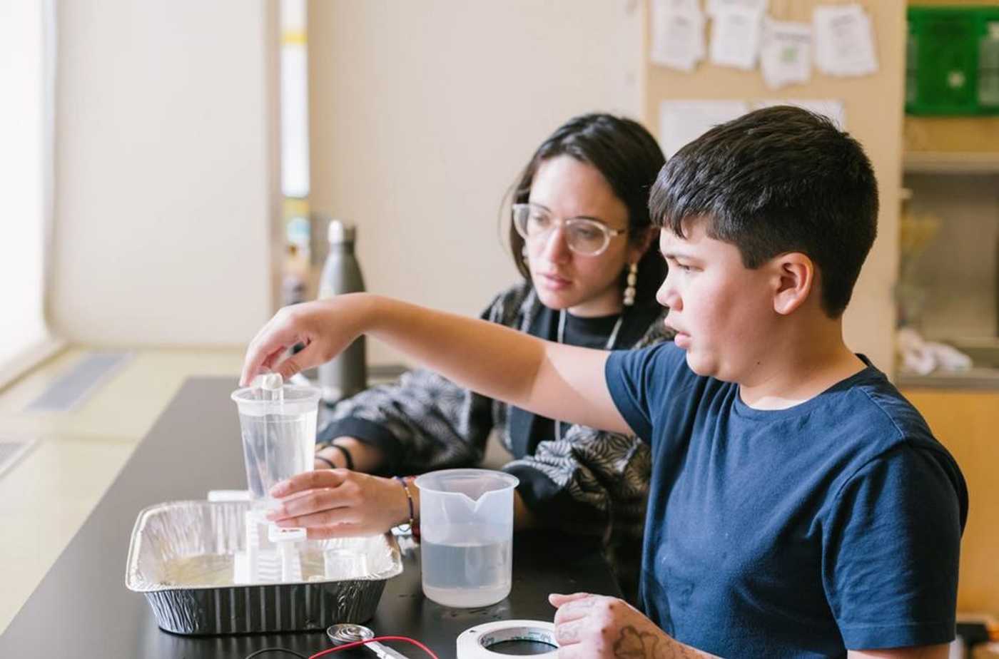 Middle school student completing a science experiment in the classroom with liquid in various beakers. 
